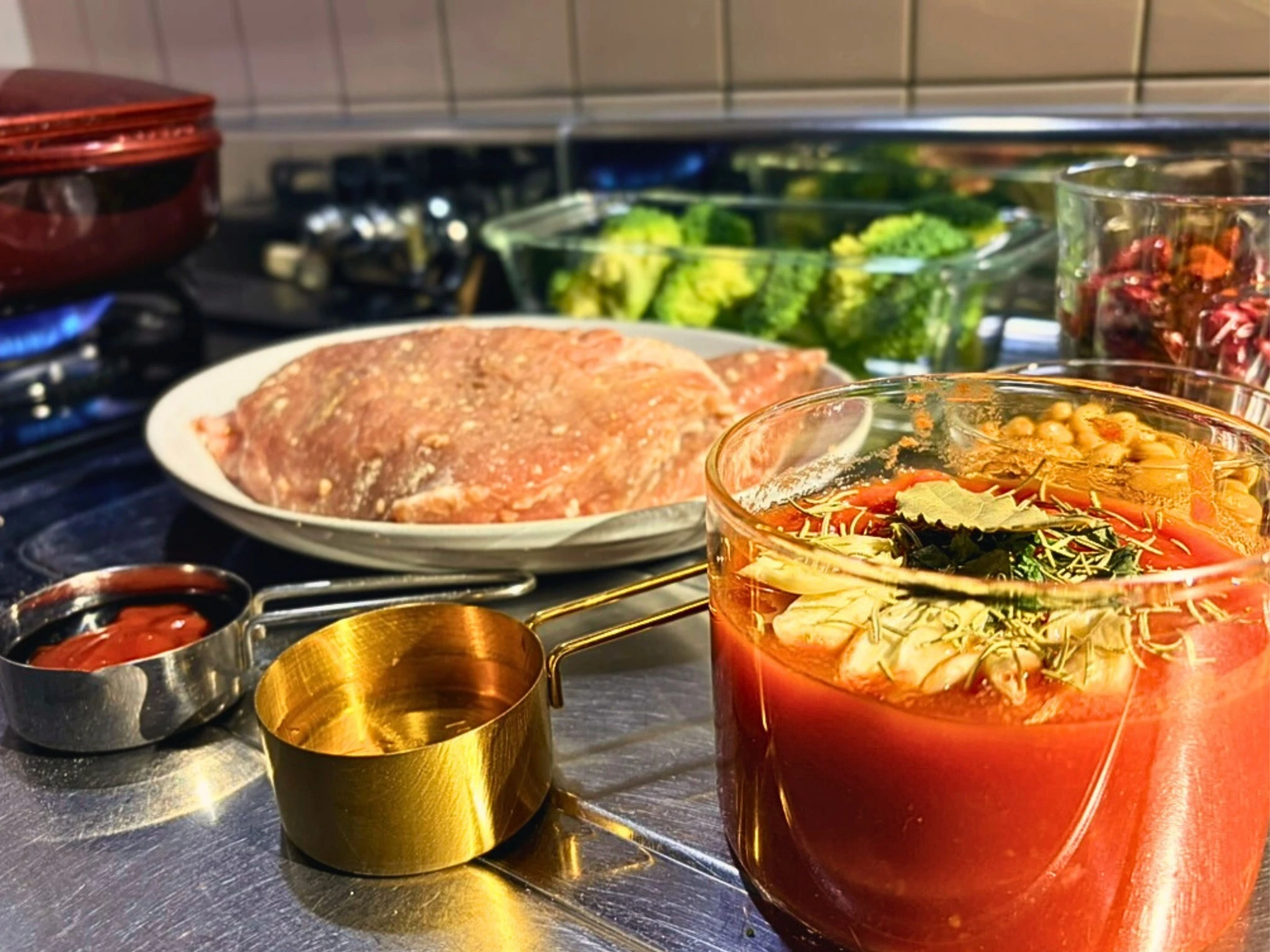 豆と野菜と豚肉の煮込みの材料と調味料。トマトベースの煮汁にハーブやにんにくが見える