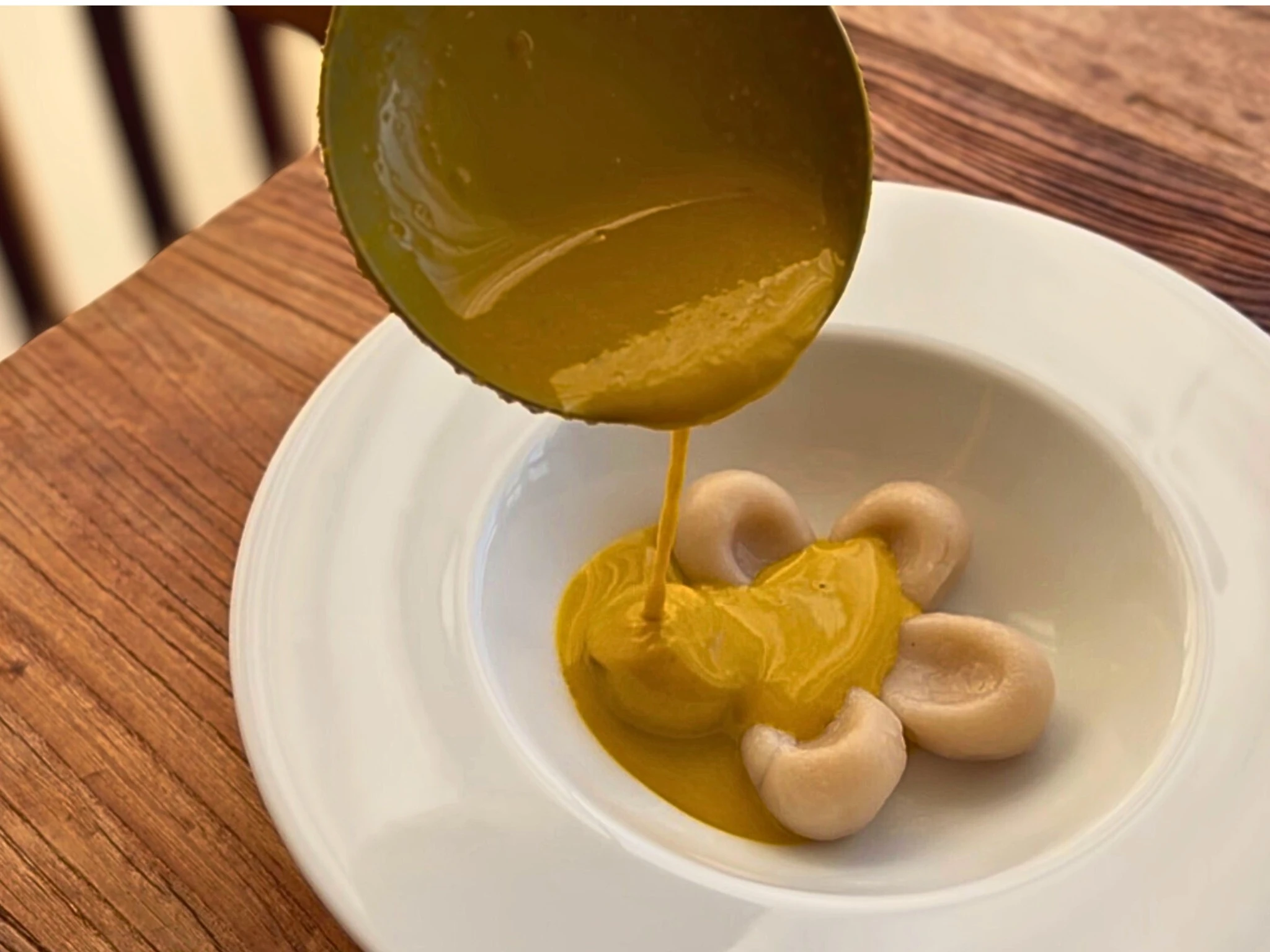 白いお皿の上の白玉団子に、かぼちゃ汁粉をそっと注いでいる瞬間