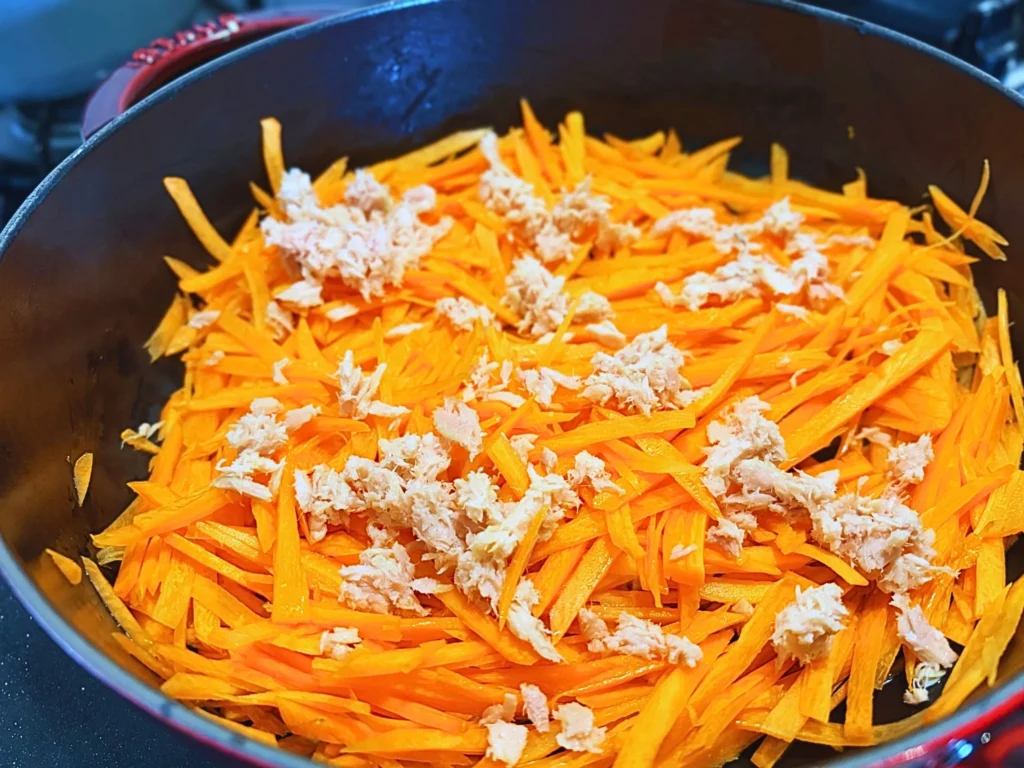 さっと炒めたにんじんにツナを散らすように加えているところ