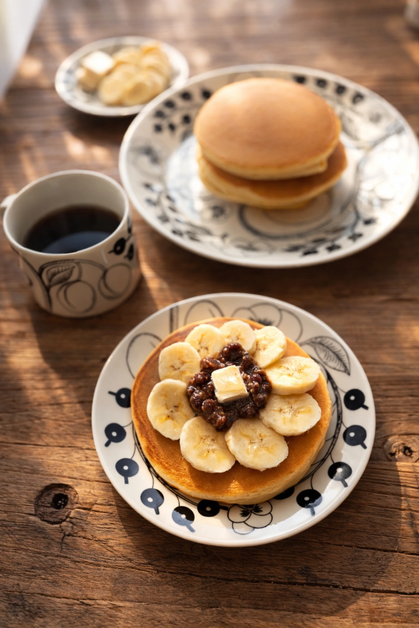 木のテーブルに並んだココナッツミルクのホットケーキとコーヒー。朝のやわらかな光の中の静かな食卓