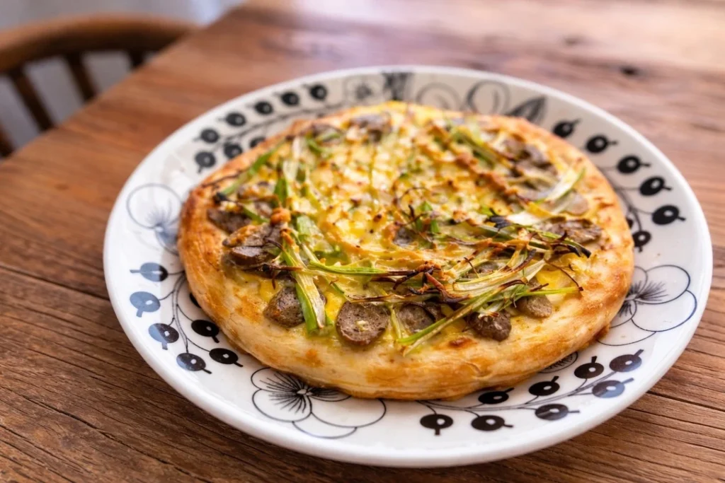 栗原はるみさんの卵ピザ。長ねぎと手作りソーセージをのせて焼き上げた、やさしい味わいの家庭料理