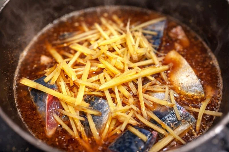 鍋でゆっくり煮込んでいるさばの味噌煮。生姜の千切りがたっぷりとのった様子